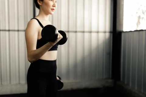 Exercise concept The sturdy woman elevating two dumbbells in her hand and doi Stock Photos