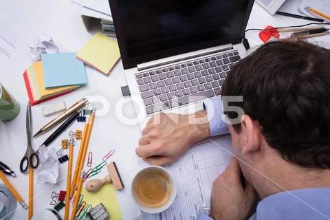 Exhausted Businessman Resting On Messy Desk With Open Laptop