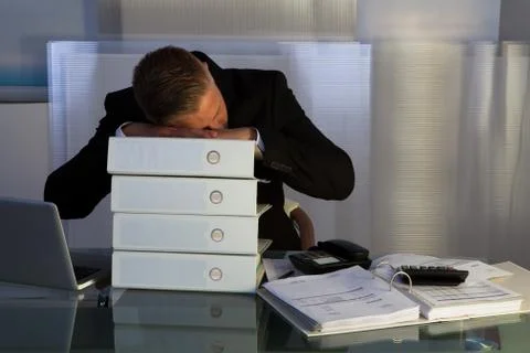 Exhausted businessman sleeping an a stack of files Stock Photos