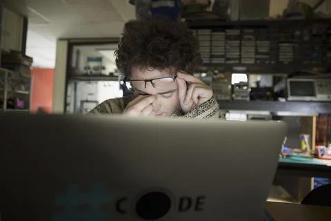 Exhausted computer programmer at laptop in dark workshop Stock Photos
