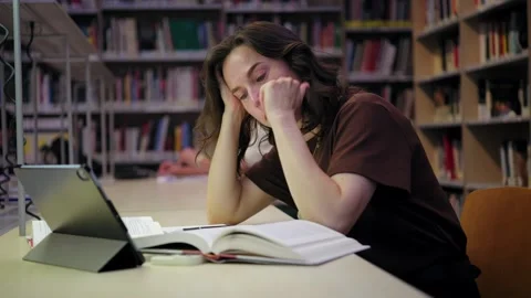 Exhausted Female Student Yawns While Studying Late in the University Library Video stock 336042364