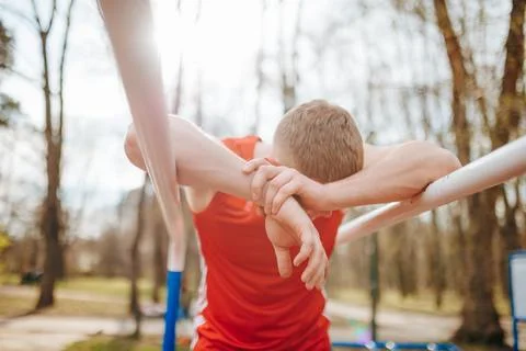 Exhausted guy in red t-shirt collapsing after a rigorous parallel bars workout. Stock Photos