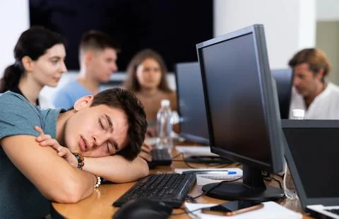 Exhausted guy student sits at table, puts head on crossed arms and sleeps after Stock Photos
