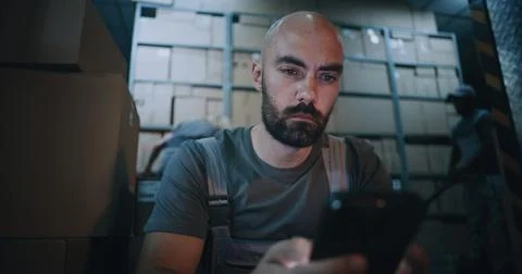 Exhausted Loader Using Smartphone, Having Rest after Hard Workday in Logistics 스톡 사진