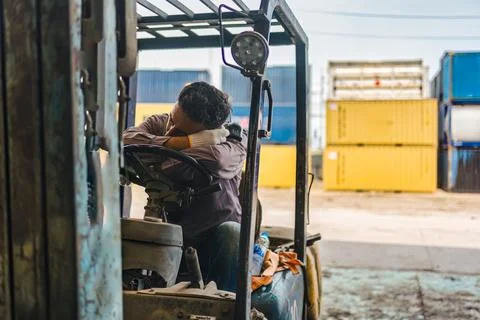 Exhausted logistics worker sleeping on forklift steering wheel in freight y.. Fotos Stock
