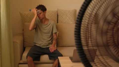 Exhausted man cooling forehead with cold water bottle during extreme heatwave at Stockbeeldmateriaal 346248401
