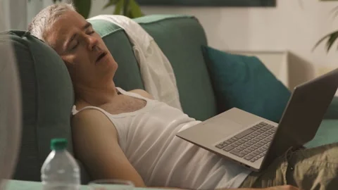 Exhausted man falling asleep on the couch during the summer heatwave Stock Footage 297860994