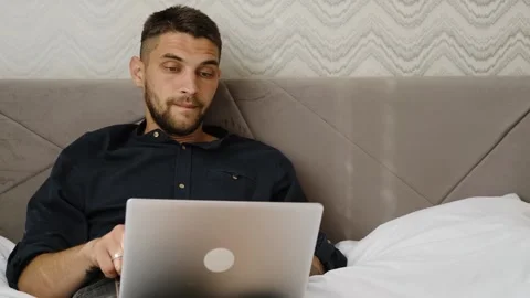 Exhausted man finishes remote work and closes his laptop while lying in bed, end Stock Footage 342543869