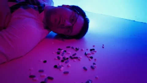 Exhausted man in formal clothes lying on the floor surrounded by pills Stock Footage 325728951