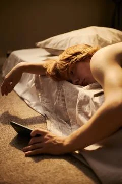 Exhausted Man Lying in Bed Looking at Smartphone Screen Fotos Stock