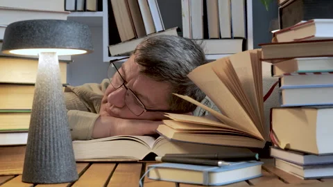 Exhausted man resting among piles of books at desk Stock Footage 336206394