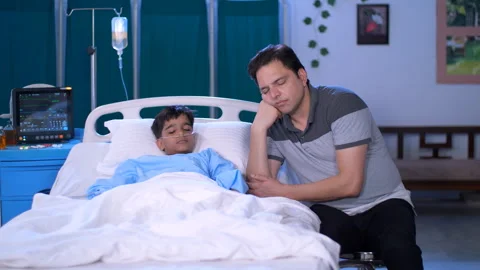 An exhausted man is resting by the bedside of his little son in hospital - ex... Stock-Footage 248814295