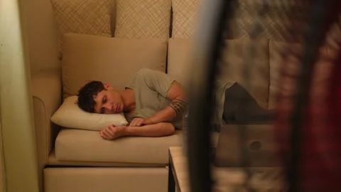 Exhausted man resting in front of electric fan after extreme heatwave at home Stockbeeldmateriaal 346248161