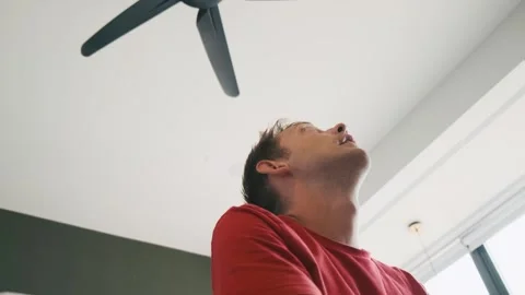 Exhausted man sitting under ceiling fan at home, cooling off during hot summer Stock Footage 278463499