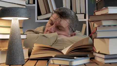 Exhausted man sleeping at desk surrounded by books during study Stock Footage 335151917