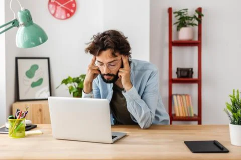 Exhausted man suffering from headache while working on his laptop. Stock Photos