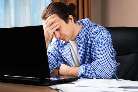 Exhausted man touching forehead while working on laptop. Concept of stress,.. Stock Photos
