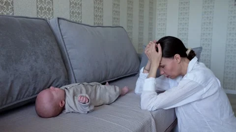 Exhausted mother puts head onto sofa near lying baby at home Stock Footage 312952464