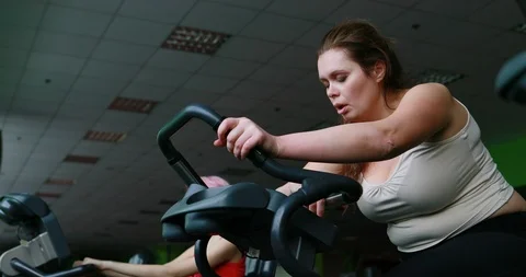 The exhausted obese woman is hardly working out on the exercise bike and sadly Stock Footage