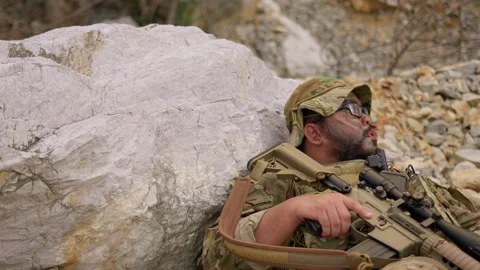Exhausted soldier with face paint rests behind a rock Stock Footage 342619410