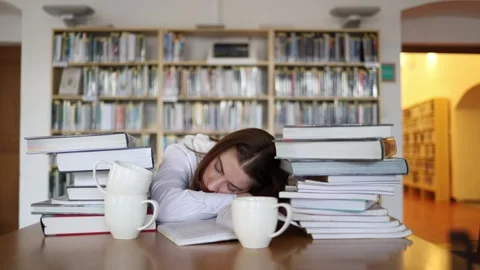 Exhausted student falls asleep over textbooks after studying in library Stock-Footage 341655792