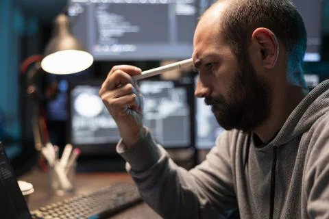 Exhausted tech freelancer leans forward holding pen to forehead Stock Photos