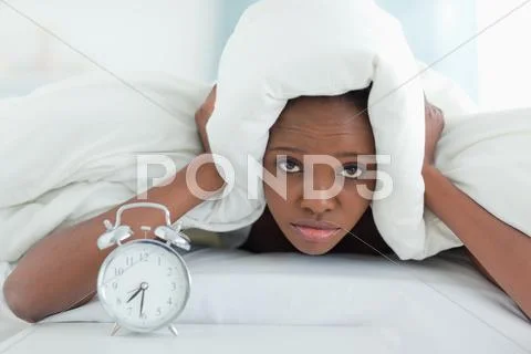 Exhausted woman covering her ears with a duvet Stock Photos