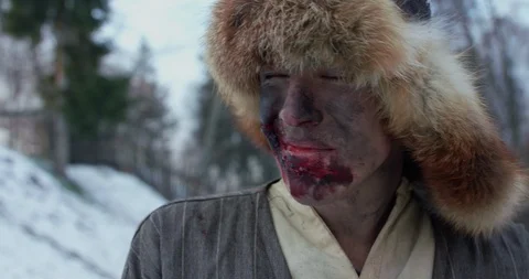 Exhausted wounded man in fur hat, all in blood, wipes himself and looks up Vídeo Stock 122298094