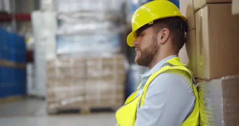 Exhausted young cargo worker sleeping leaning on large container in warehouse Stock Footage 151398582