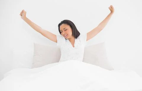 Exhausted young dark haired model stretching in her bed Stock Photos