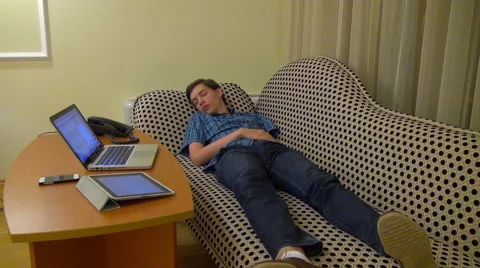 Exhausted young man asleep on a couch at work with laptop Stock Footage 68386758