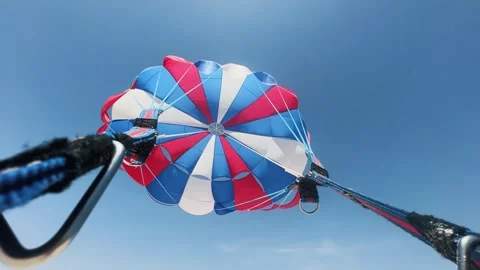 Exhilarating view of a vibrant red, white, and blue parasail hovering high ag Stock Footage 312733632