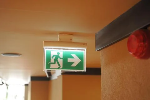 Exit sign hangs on the wall in a building hallway Stock Photos