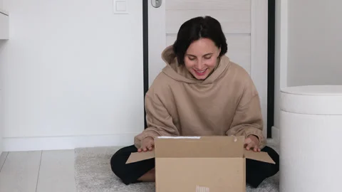 Exited woman checking a parcel, looking inside the open a cardboard box at home Stock Footage 255590374