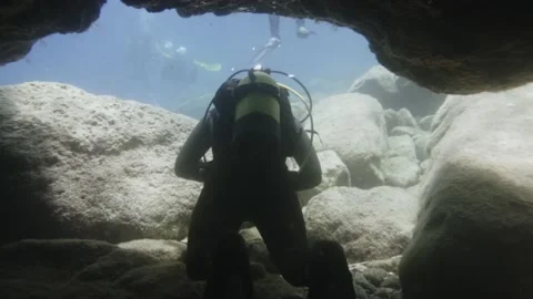 Exiting an underwater cave with a diver turning towards camera after completion Stock Footage 238838010