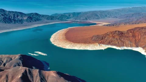 Expansive arid lake curves through desert mountains under clear blue sky drone Stock Footage 343696222