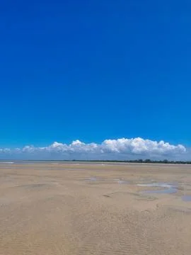 Expansive Coastal Sand Flat Beneath Vibrant Blue Sky and Fluffy Clouds Stock Photos