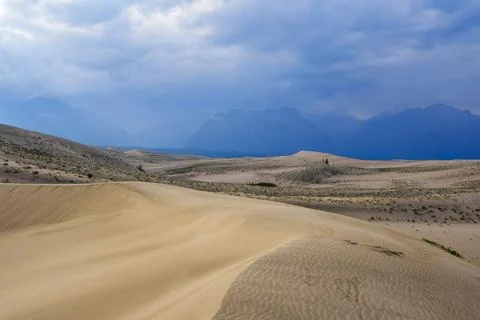 Expansive desert dunes under a dramatic sky with distant mountains Stock Photos