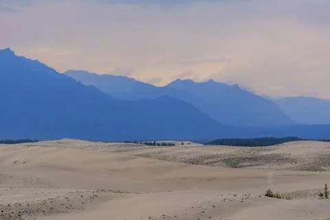 Expansive desert dunes under a dramatic sky with distant mountains Stock Photos
