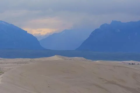 Expansive desert dunes under a dramatic sky with distant mountains Stock Photos