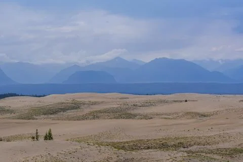 Expansive desert dunes under a dramatic sky with distant mountains Foto stock
