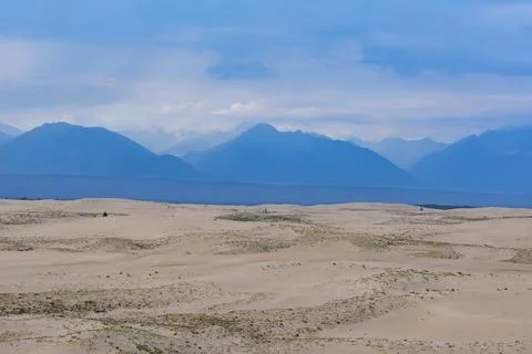 Expansive desert dunes under a dramatic sky with distant mountains Foto stock