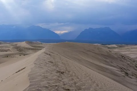 Expansive desert dunes under a dramatic sky with distant mountains Stock Photos