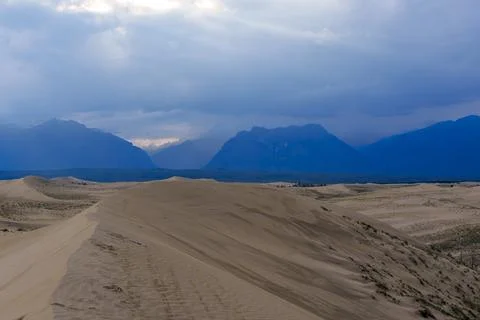 Expansive desert dunes under a dramatic sky with distant mountains Stock Photos