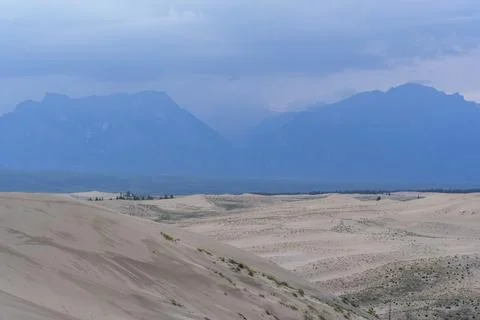 Expansive desert dunes under a dramatic sky with distant mountains Stock Photos