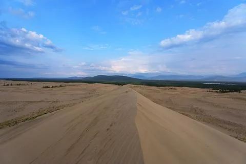 Expansive desert dunes under a dramatic sky with distant mountains Stock Photos