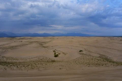 Expansive desert dunes under a dramatic sky with distant mountains Stock Photos