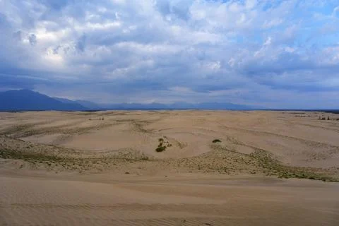 Expansive desert dunes under a dramatic sky with distant mountains Stock Photos