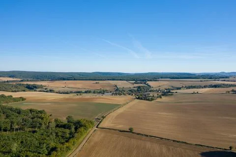 Expansive fields and distant village under blue sky Stock Photos