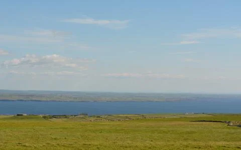 Expansive Green Fields and Tranquil Sea Meet Under a Bright Blue Sky Stock Photos